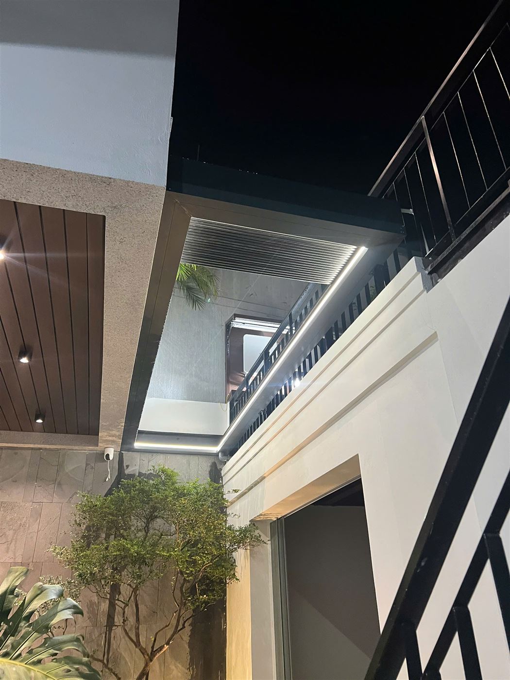Mái nhôm xếp tự động trên giếng trời có đèn LED và cây xanh bên dưới